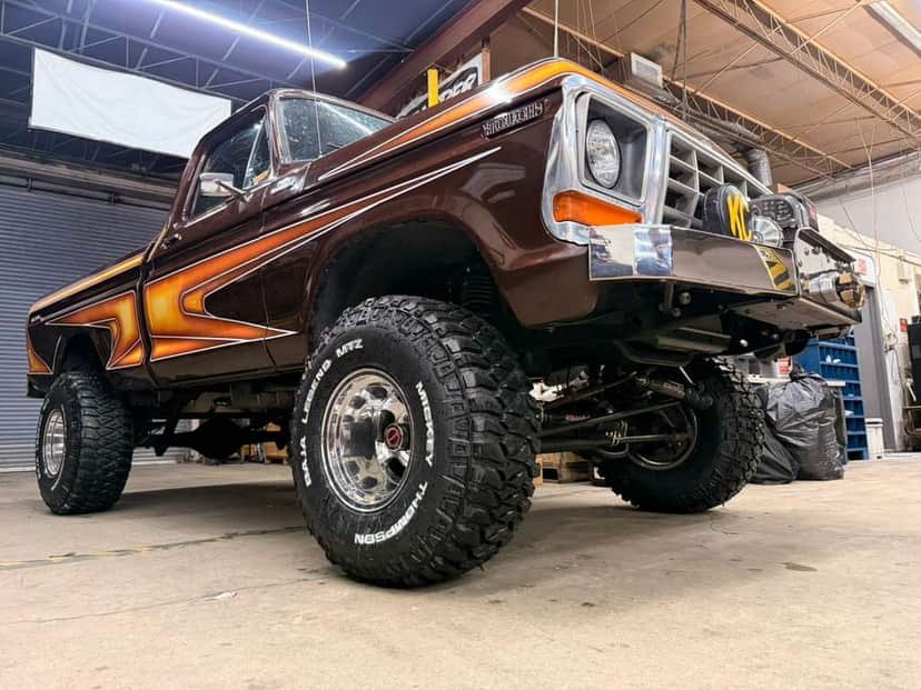 Low-angle view of Brownie inside the shop, showing the lift, the Mickey Thompson tires, and the seventies stripe package