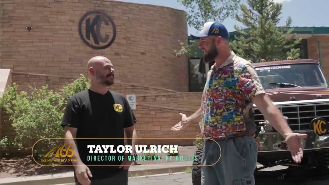 Taylor Ulrich and Solomon talking in front of the KC HiLiTES stone monument, the on-screen name plate reading Director of Marketing, KC HiLiTES, with Brownie's front bumper and its KC light at the right of frame.